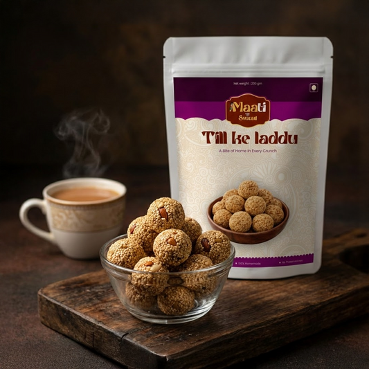 Packaged Tilkhe Laddu with a bowl of laddus and a cup of tea on a wooden surface.